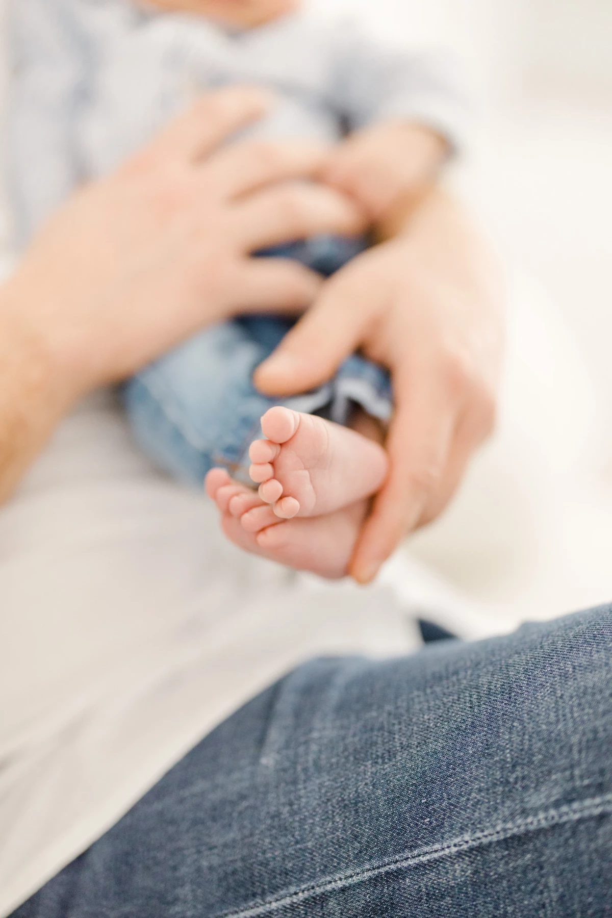 Séance naissance en studio : petits pieds de bébé tenus délicatement dans les mains de maman, instant de tendresse et douceur