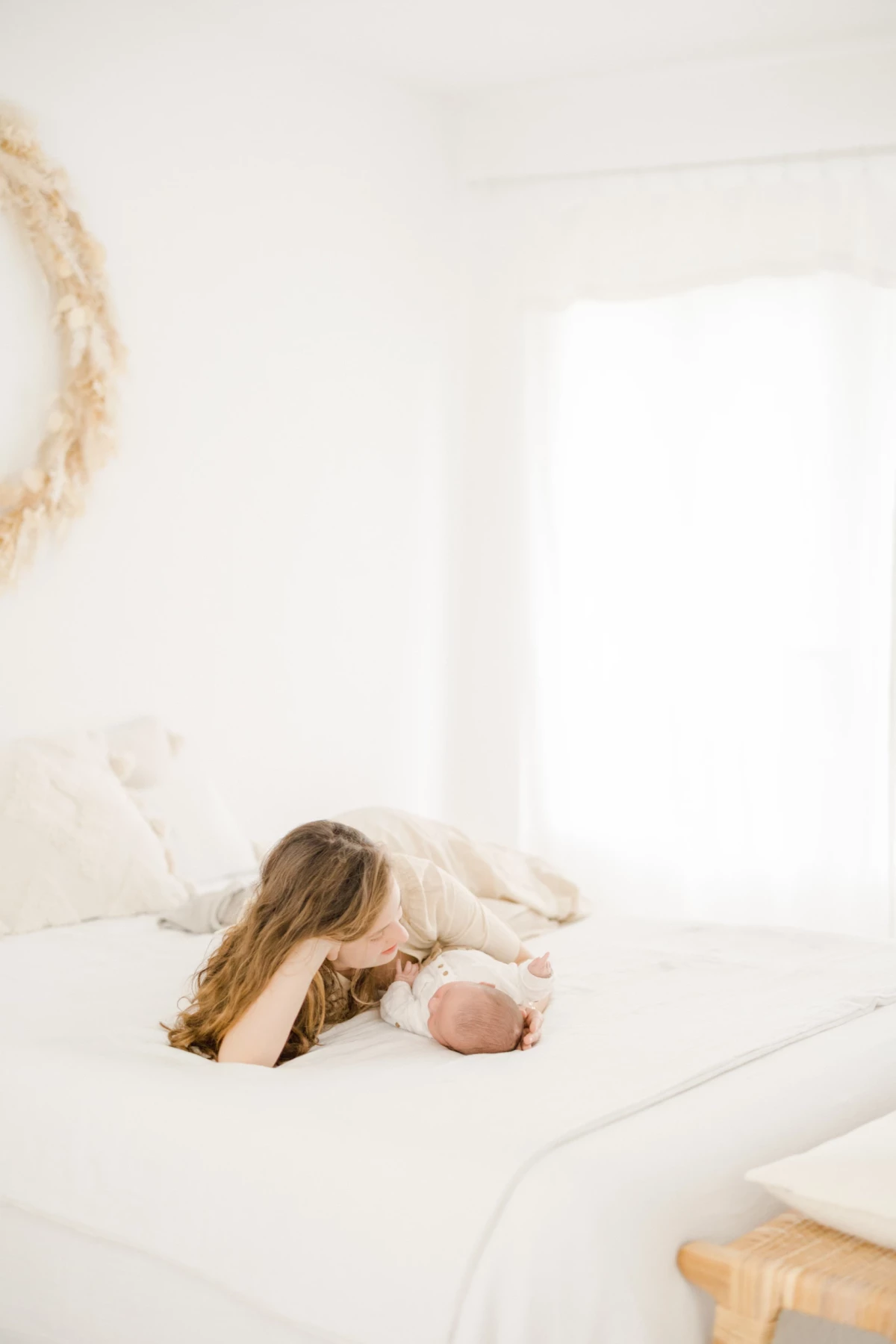Séance nouveau-né en studio : maman se penche tendrement vers son bébé allongé sur un lit blanc, instant de douceur infinie