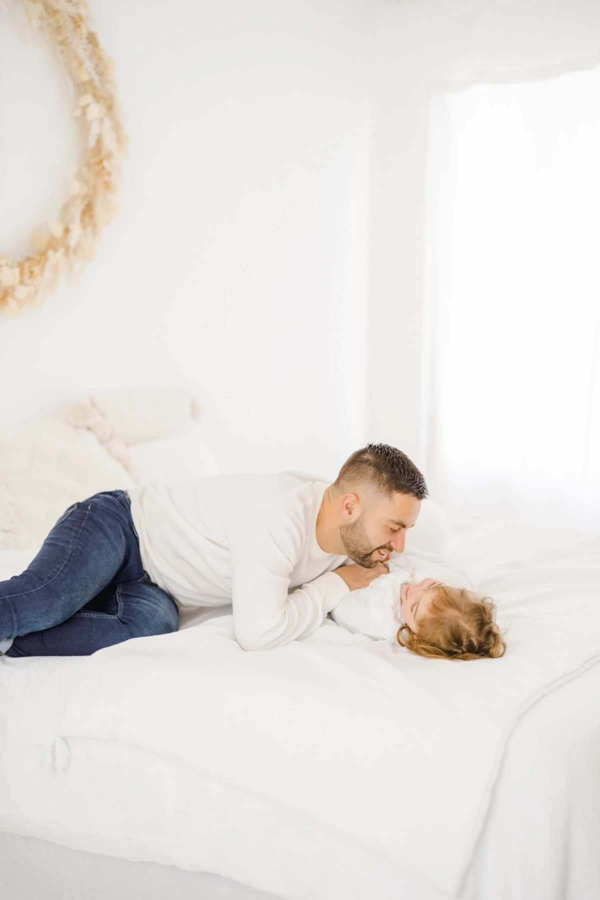 Séance naissance au studio : papa allongé partage un instant de complicité tendre avec son bébé sur un lit blanc