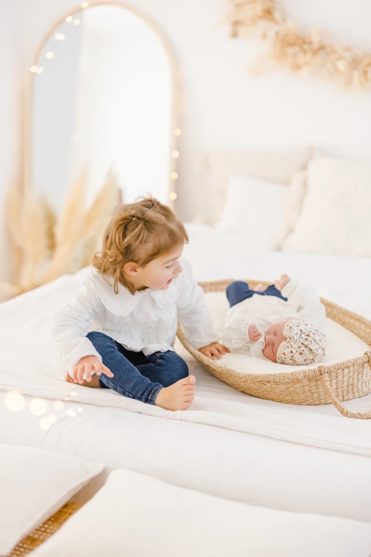Séance naissance au studio : grande sœur observe son nouveau-né avec tendresse dans un décor blanc et lumineux en Vendée