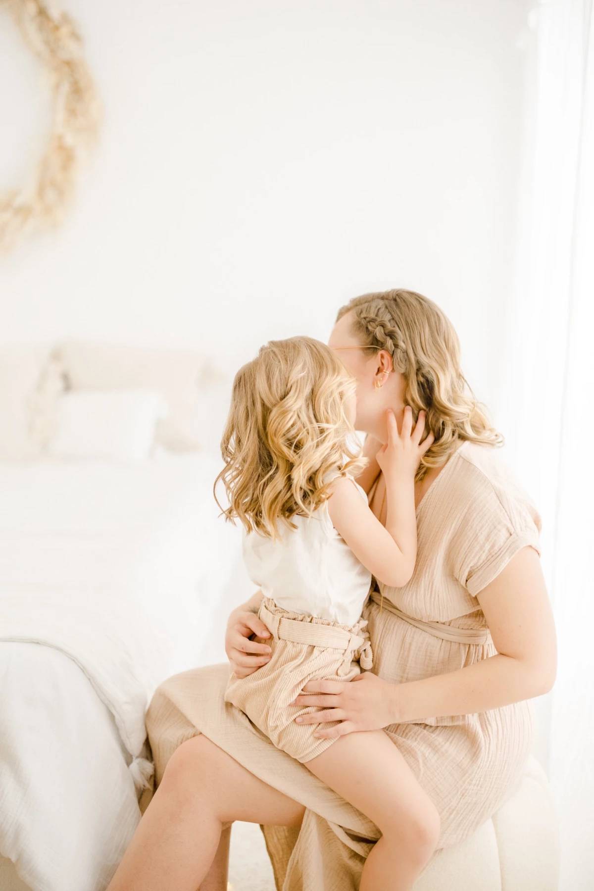 Séance grossesse en famille au studio : enfant embrasse tendrement sa maman dans une lumière douce et naturelle sur fond blanc