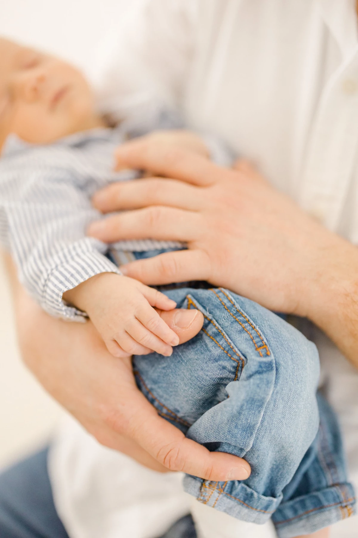 Séance naissance au studio : mains de parents et grand frère posées avec tendresse sur bébé, moment de complicité familiale