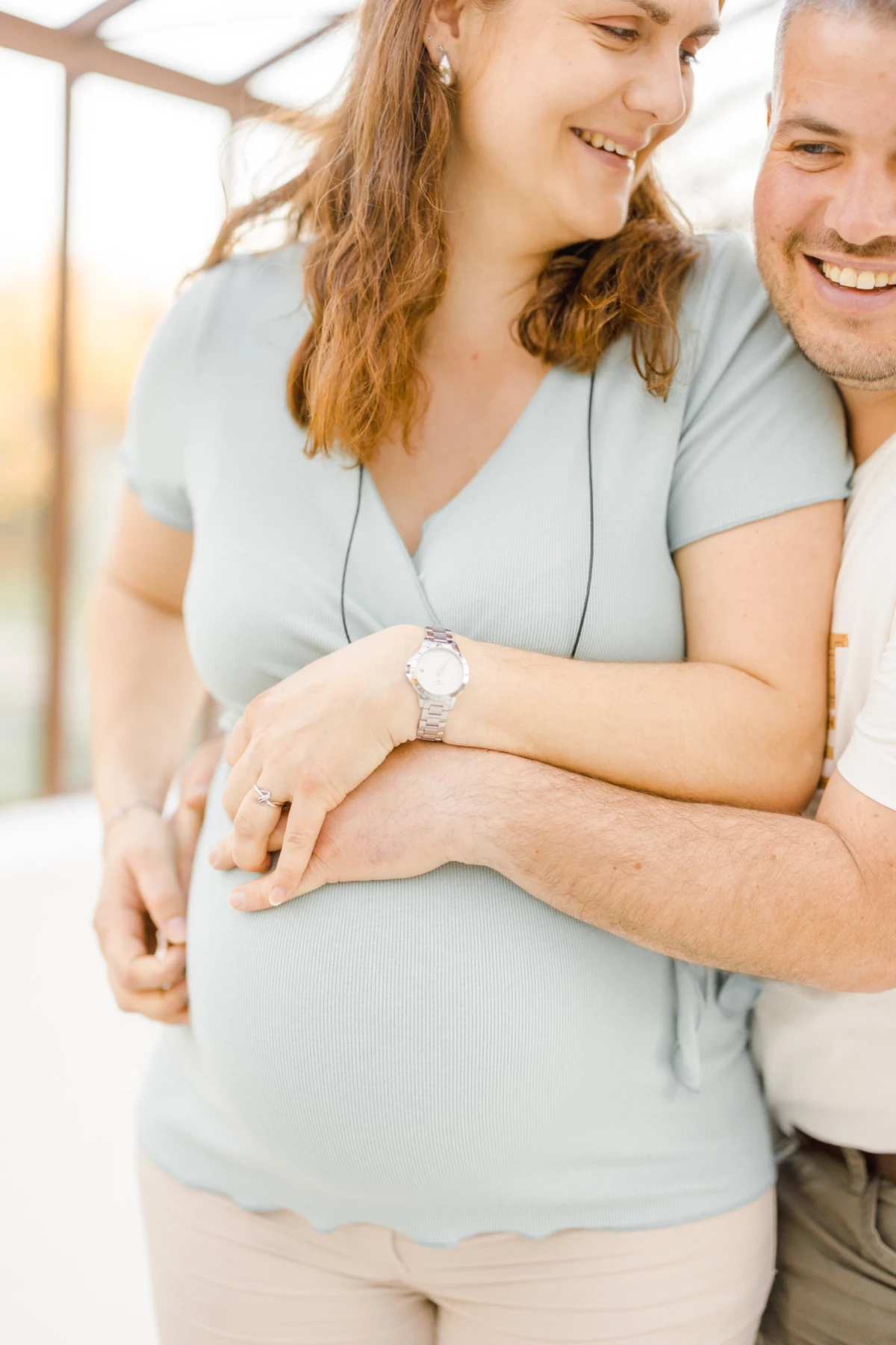 Séance grossesse en extérieur : couple enlacé partage un moment de tendresse et complicité dans une verrière lumineuse