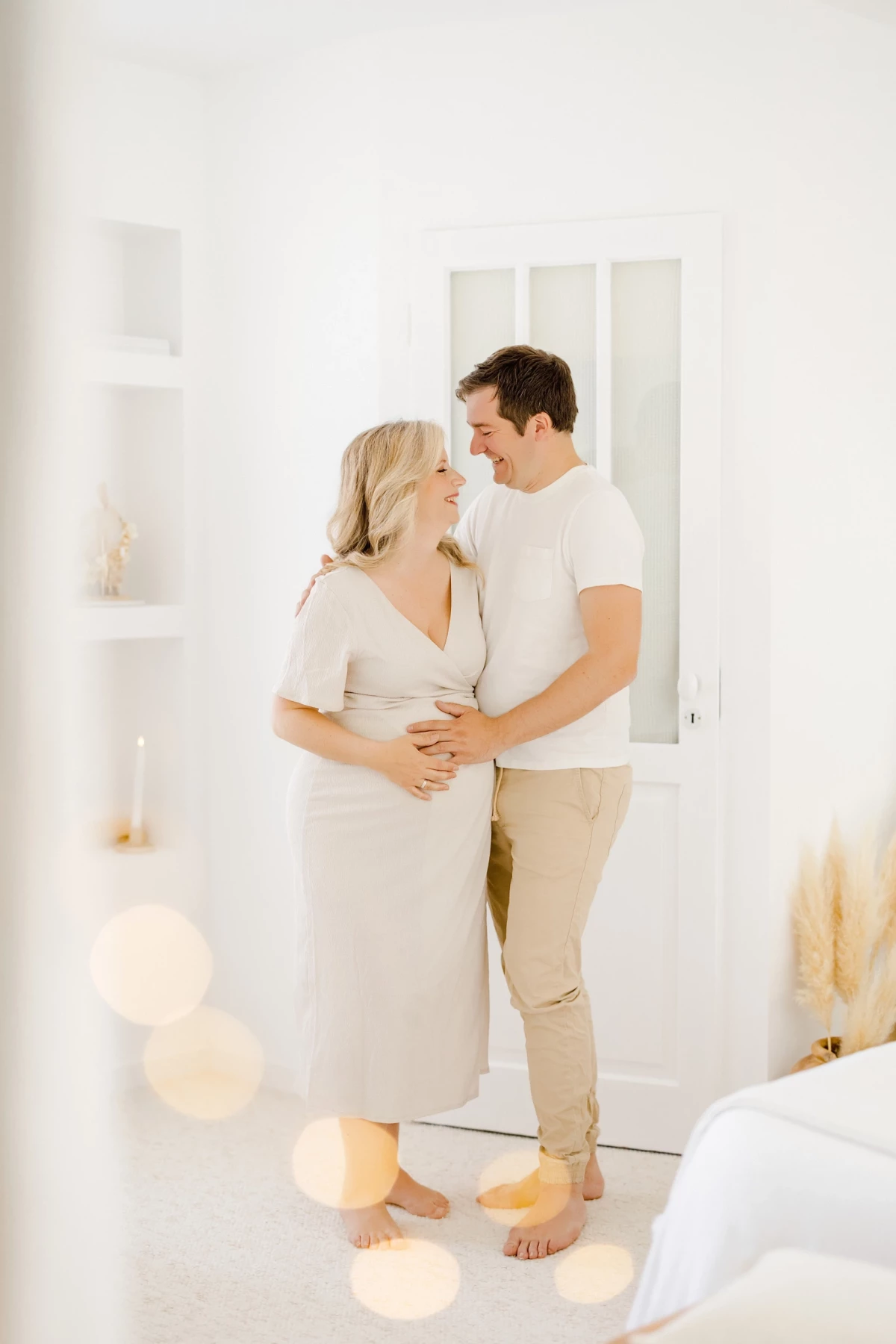 Séance grossesse au studio : couple complice entourant le ventre rond dans une ambiance blanche et lumineuse, instant de tendresse