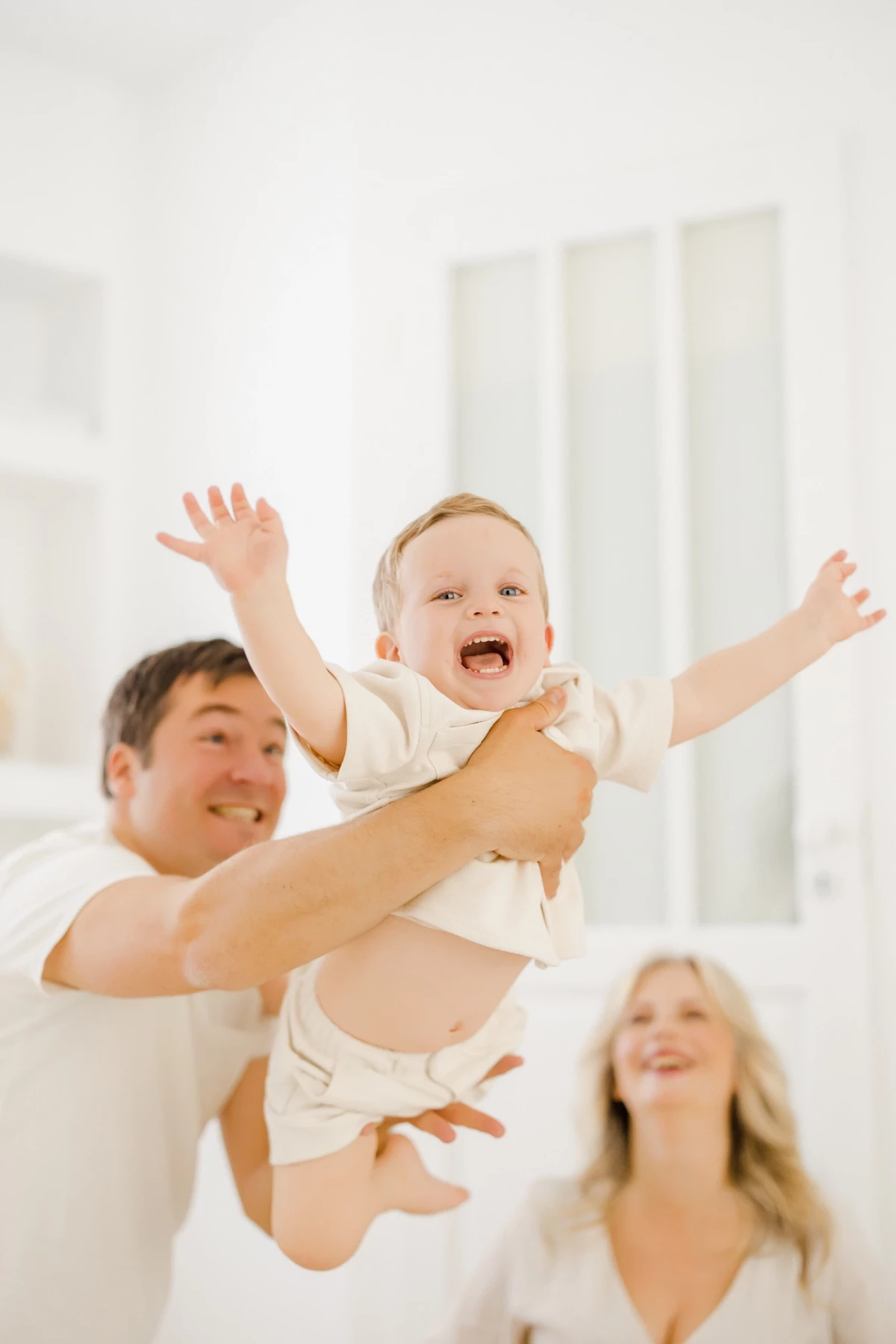 Séance famille au studio : parents et bébé partagent un moment de complicité joyeuse dans une ambiance lumineuse et épurée