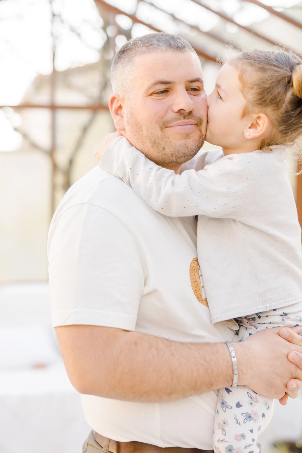 Séance famille en extérieur : père et fille partagent un moment de tendresse dans une verrière lumineuse en Vendée