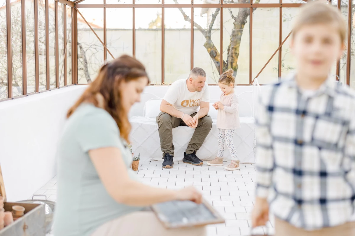 Séance grossesse famille en verrière : parents attendant bébé avec leurs deux enfants dans une atmosphère lumineuse et intemporelle