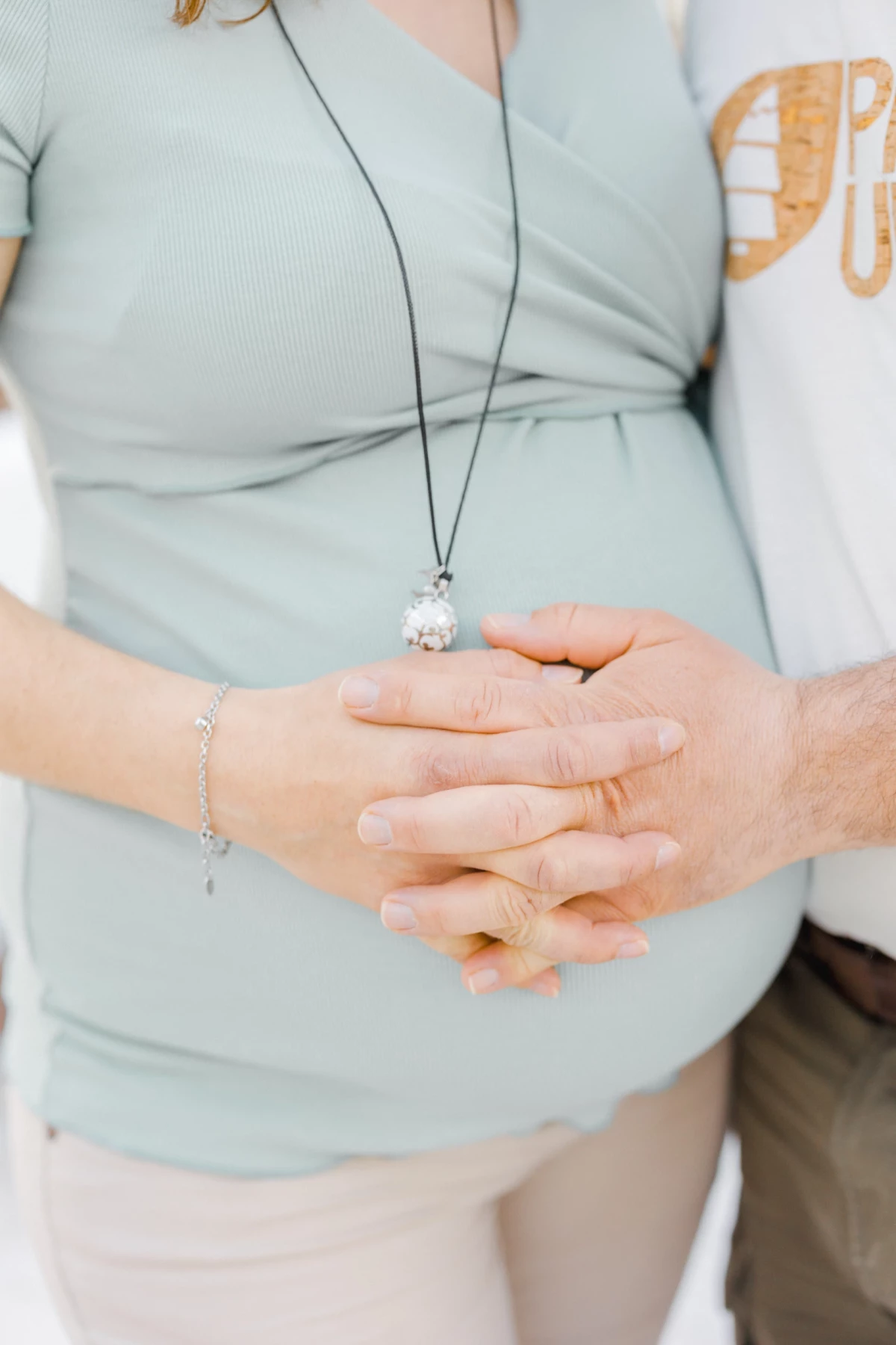 Séance grossesse en studio : future maman et son enfant posent leurs mains enlacées sur son ventre rond, geste de tendresse familiale