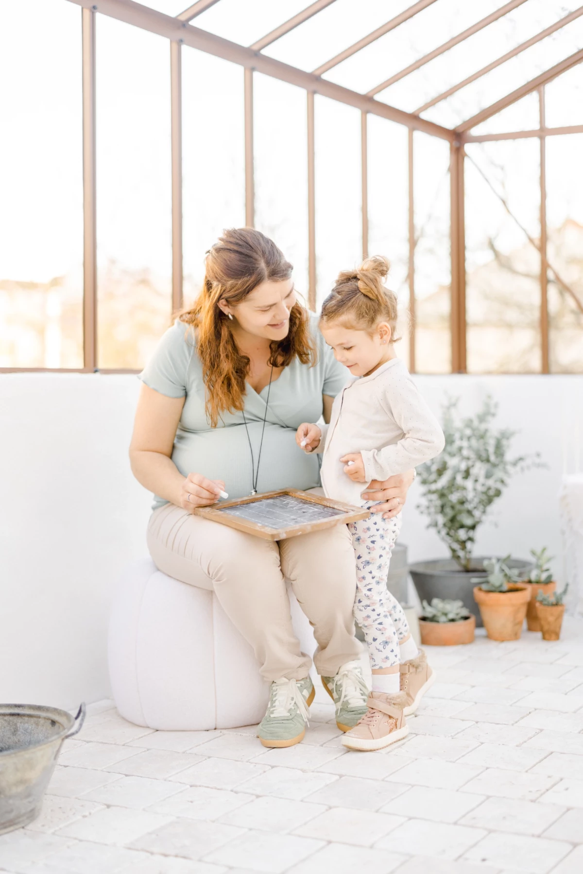 Séance grossesse en verrière : future maman partage un livre avec sa fille, instant de complicité familiale dans une lumière douce