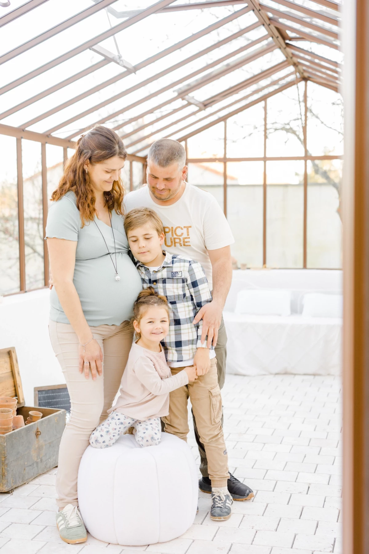 Séance grossesse famille en verrière : parents et enfants réunis dans une lumière douce et naturelle, moment de tendresse partagée