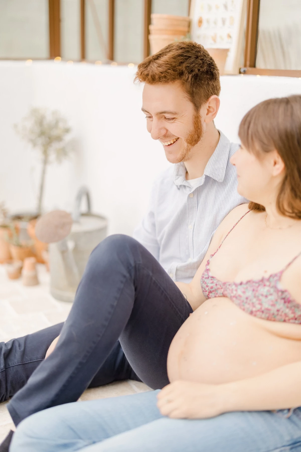 Séance grossesse au studio : couple complice assis au sol, future maman au ventre rond et futur papa partagent un moment de tendresse