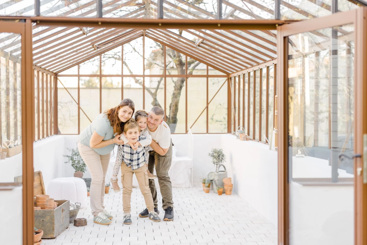 Séance grossesse en famille : parents et enfants réunis dans une verrière lumineuse, instant de complicité et de tendresse partagée