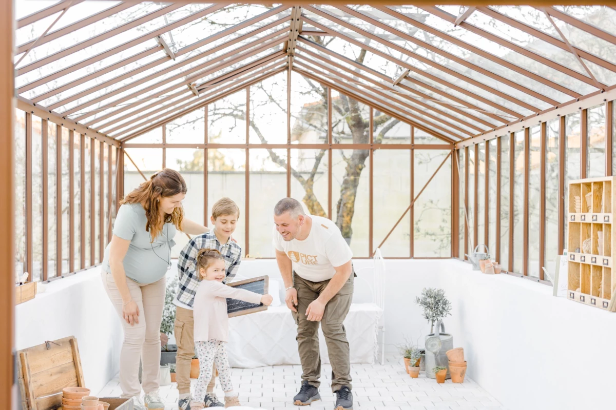 Séance grossesse famille dans une verrière lumineuse : parents et enfant partagent un moment de complicité dans un décor épuré