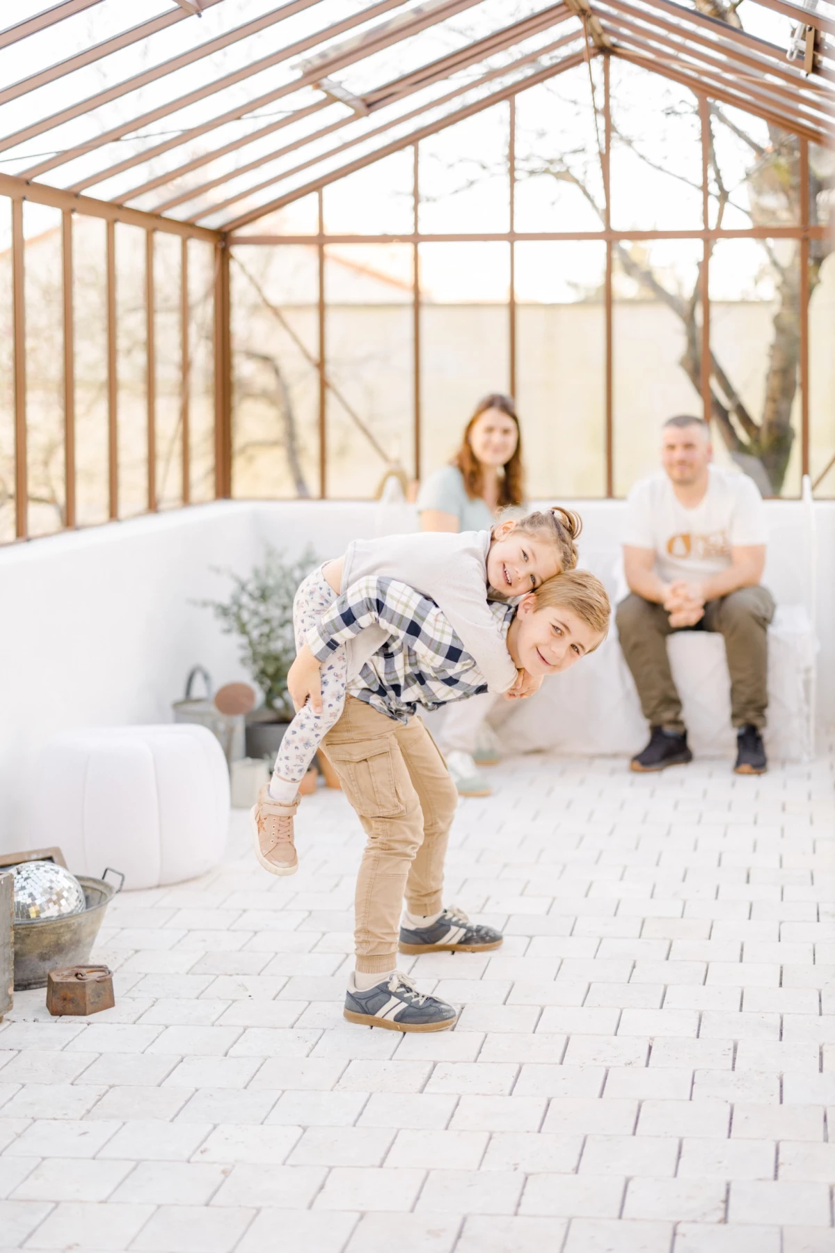 Séance grossesse famille en verrière : deux enfants jouent devant leurs parents dans une atmosphère lumineuse et douce
