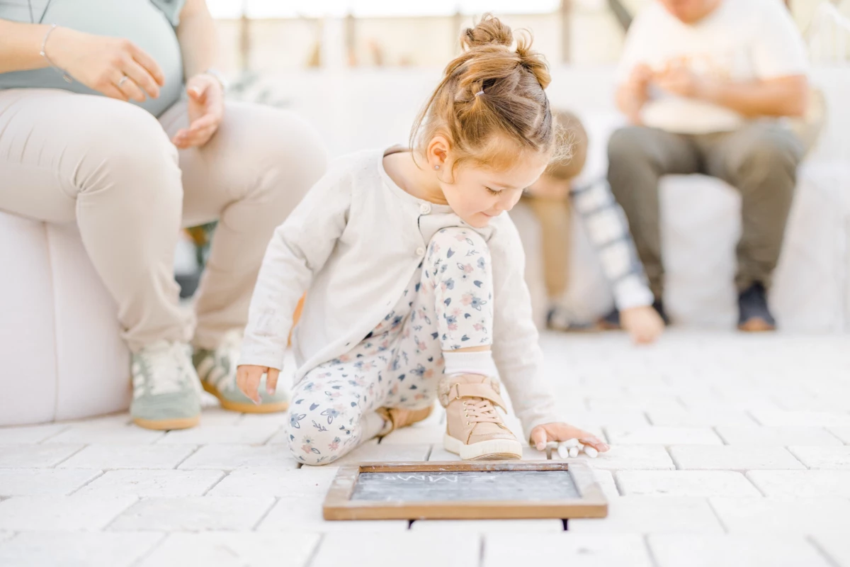 Séance grossesse en studio : petite fille joue avec une tablette pendant que ses parents attendent bébé dans une ambiance de douceur