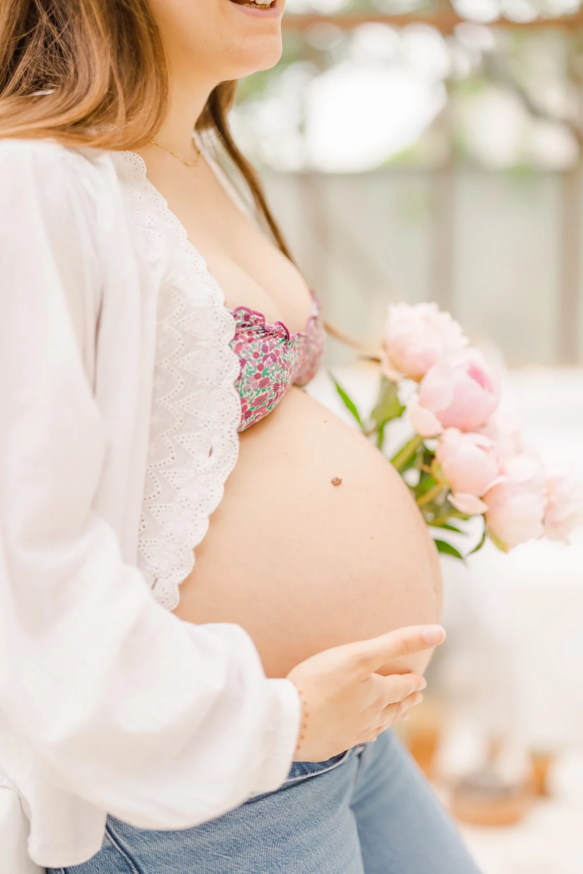 Séance grossesse en extérieur : future maman tient un bouquet de pivoines roses contre son ventre rond dans une lumière douce