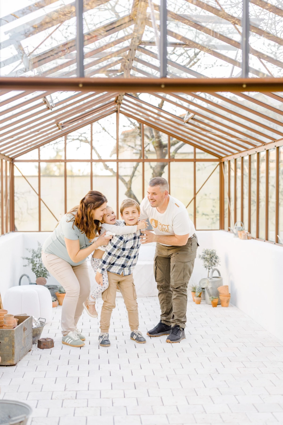 Séance grossesse famille en verrière : parents et enfant partagent un moment de complicité joyeuse dans un studio lumineux blanc.