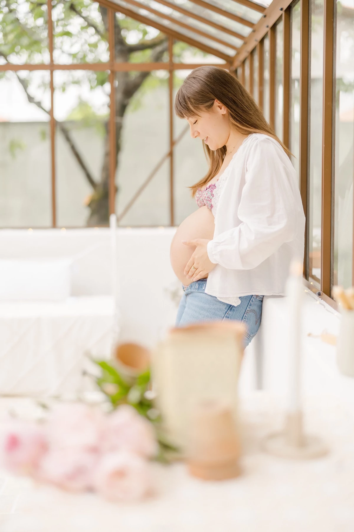 Séance grossesse au studio : future maman caresse tendrement son ventre dans une verrière lumineuse, ambiance douce et naturelle