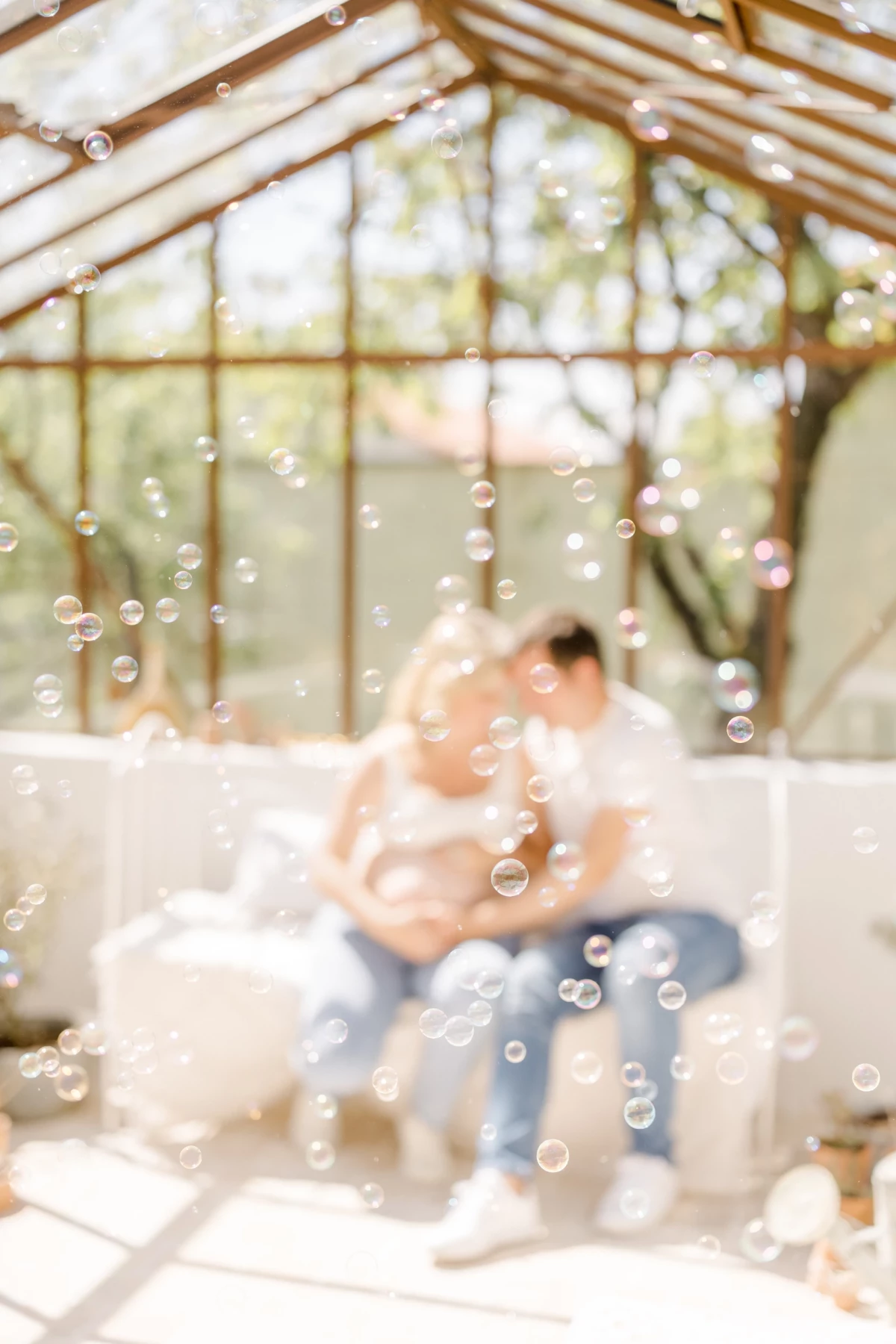 Séance famille au studio : parents et enfant partagent un moment de tendresse dans une verrière lumineuse, ambiance douce et bulles