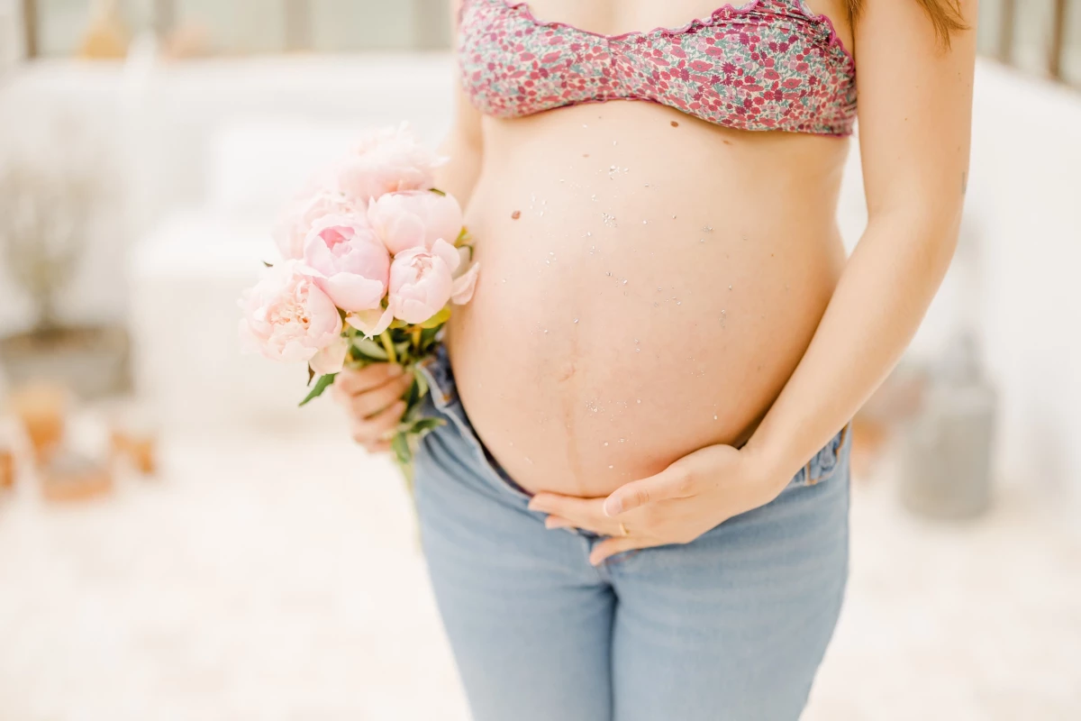 Séance maternité en extérieur : future maman tient un bouquet de fleurs roses, caressant son ventre rond dans une lumière douce