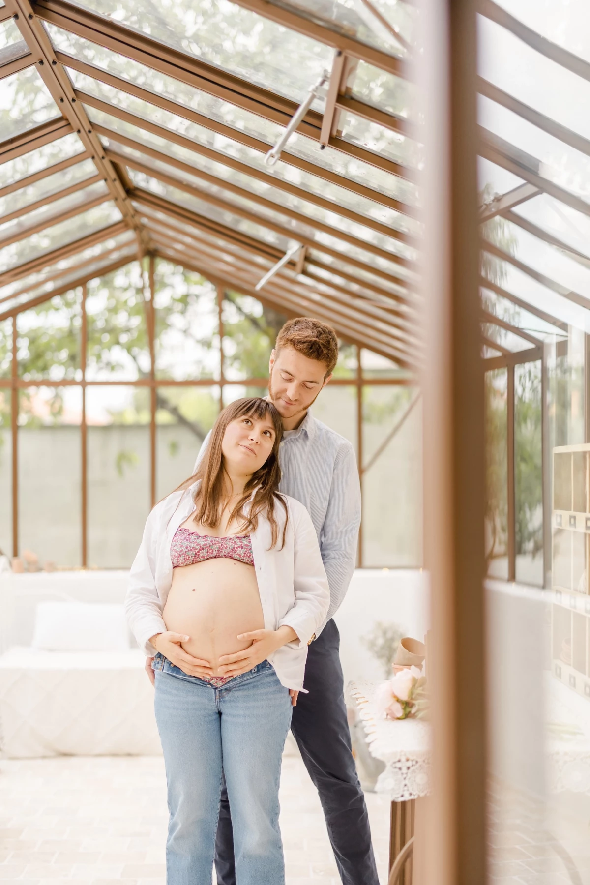 Séance grossesse en verrière : couple complice, future maman caresse son ventre rond dans une lumière douce et naturelle