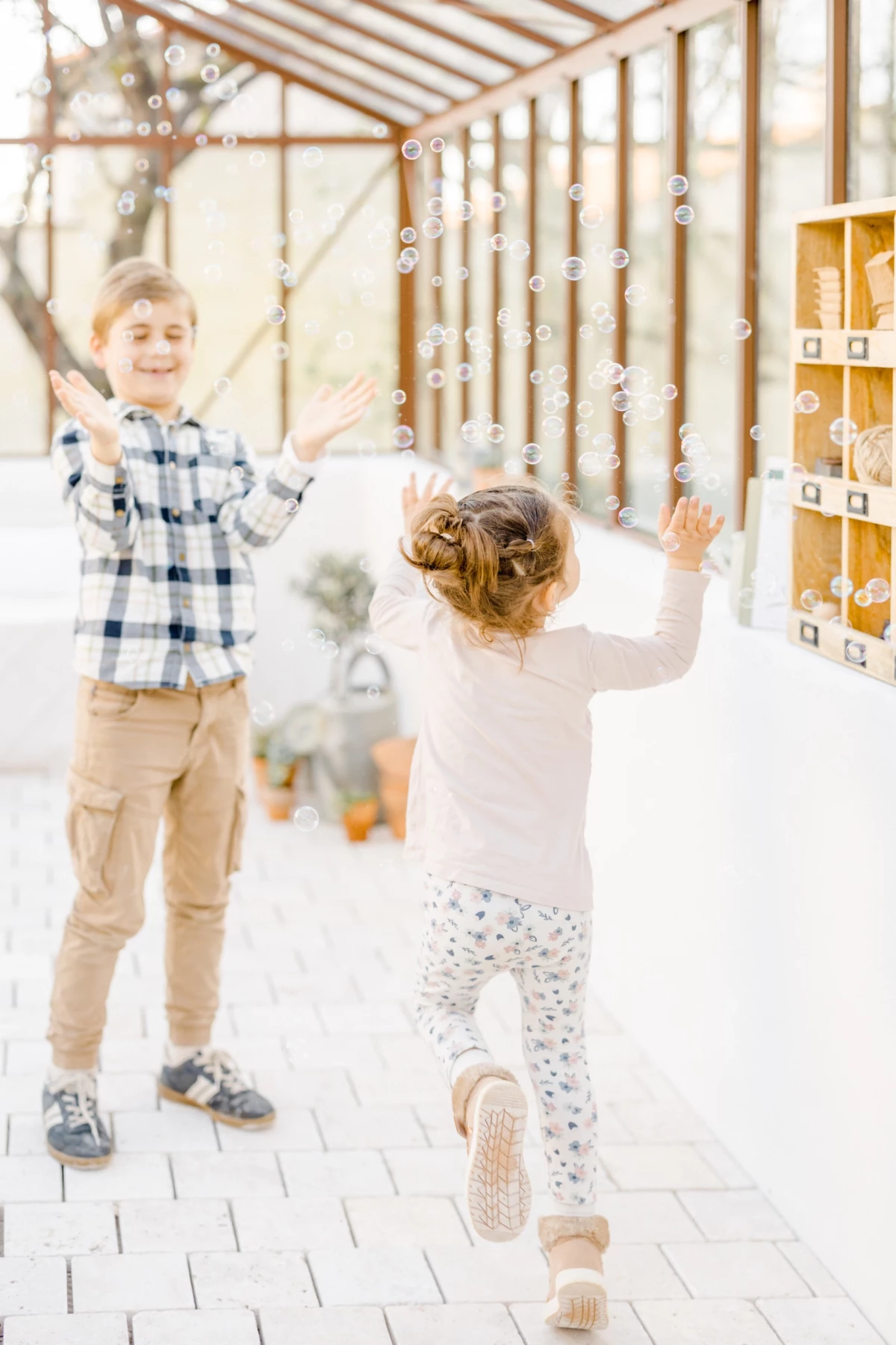 Séance famille au studio : deux enfants jouent joyeusement dans une verrière décorée pour Noël, ambiance lumineuse et festive