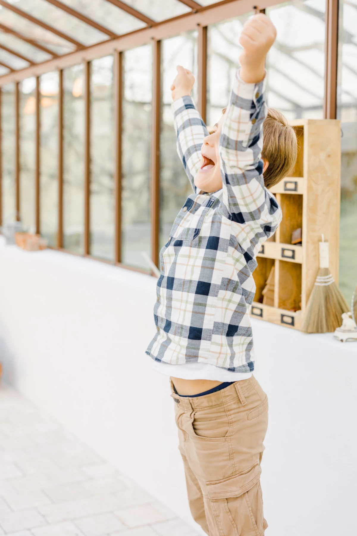 Séance grossesse en studio : enfant lève les bras avec joie dans une verrière lumineuse, instant de bonheur familial
