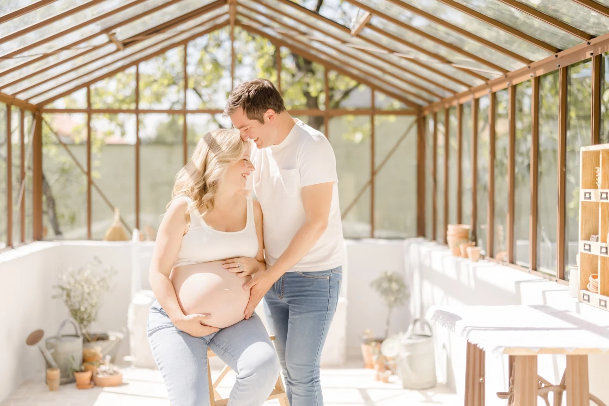 Séance grossesse en verrière : couple complice s'embrassant tendrement, future maman en crop top beige dans une lumière douce
