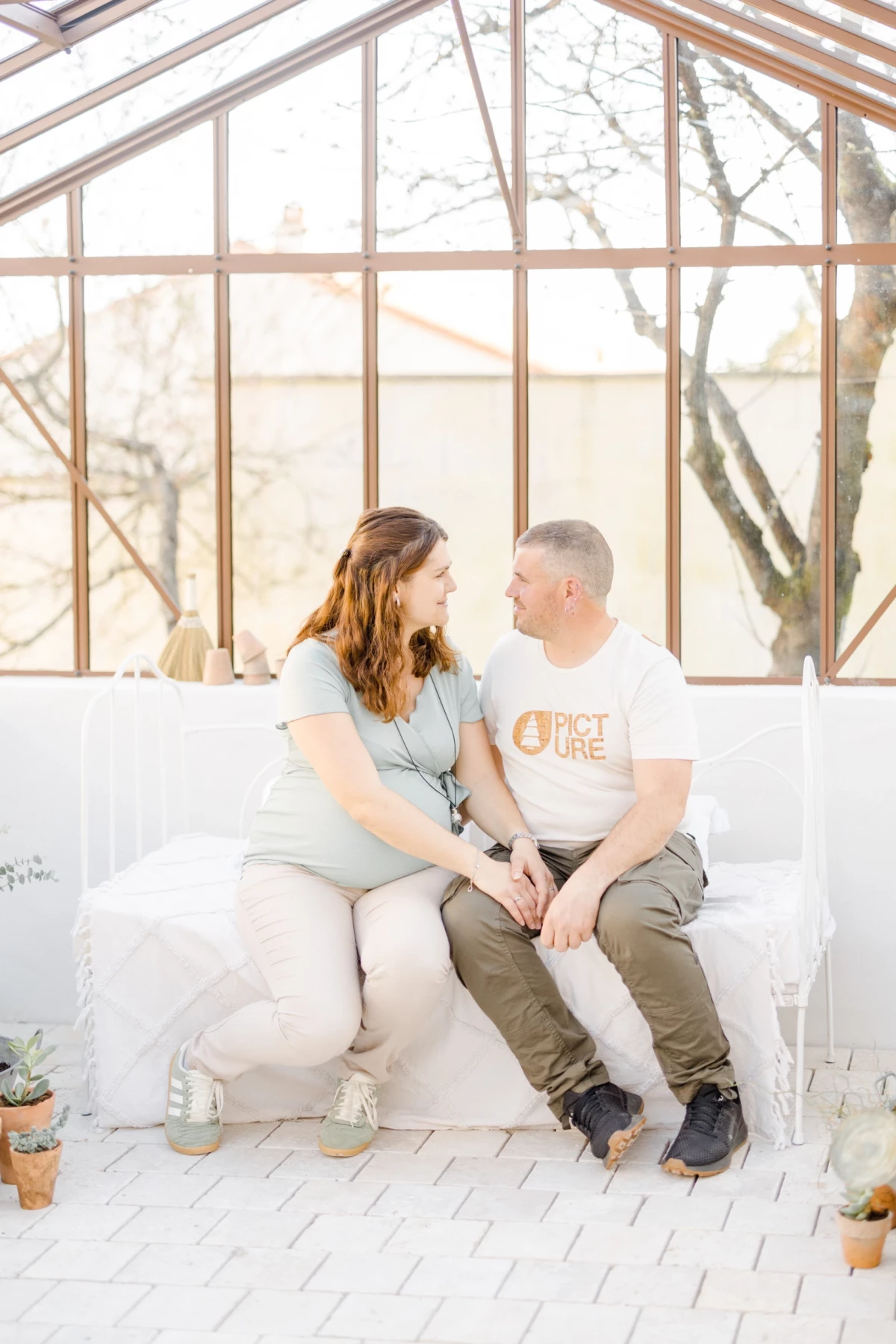 Séance grossesse en verrière : couple complice assis main dans la main dans une atmosphère lumineuse et naturelle en Vendée