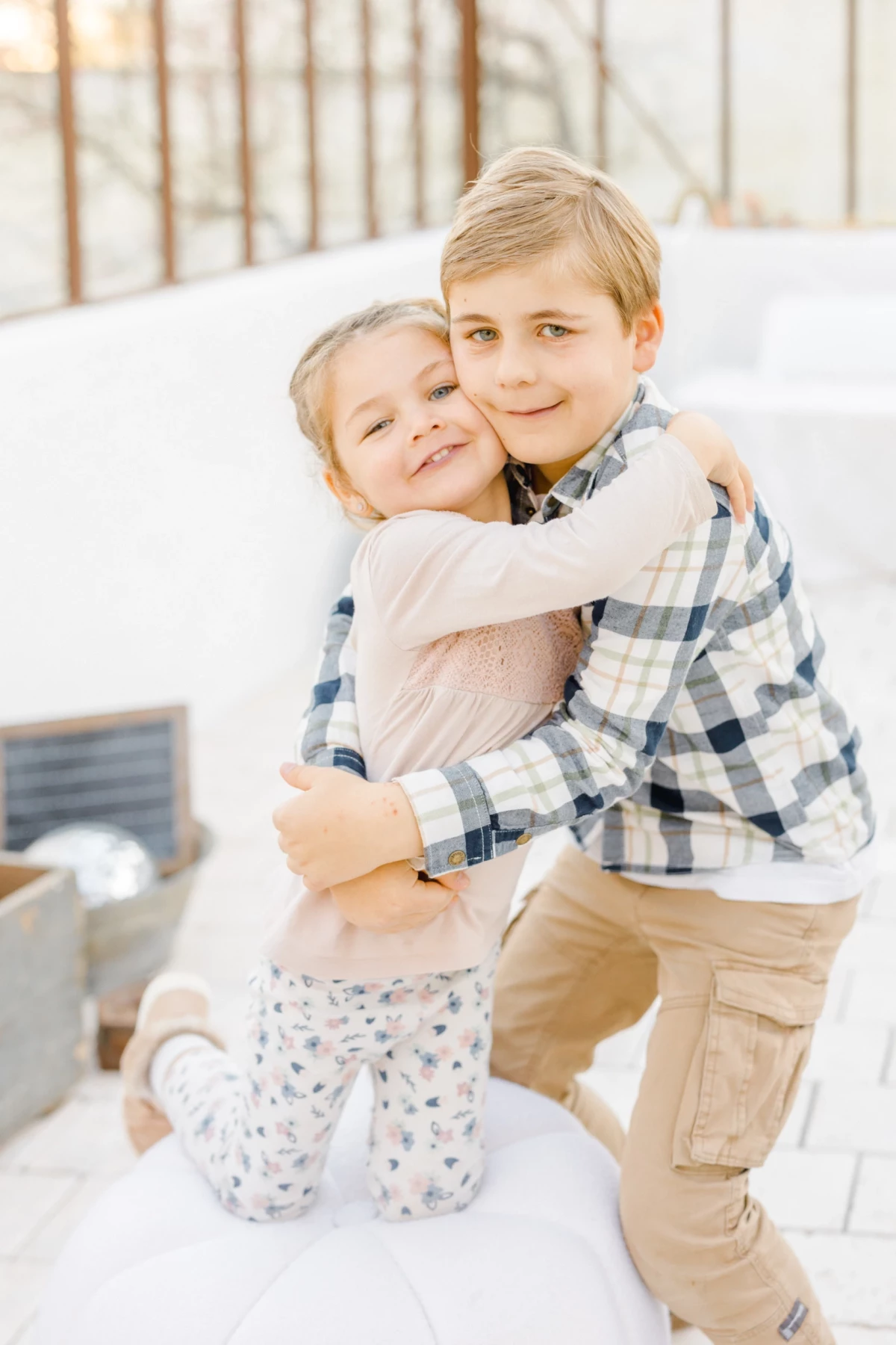 Séance grossesse en studio : frère et sœur s'enlacent tendrement dans une verrière lumineuse, moment de complicité fraternelle