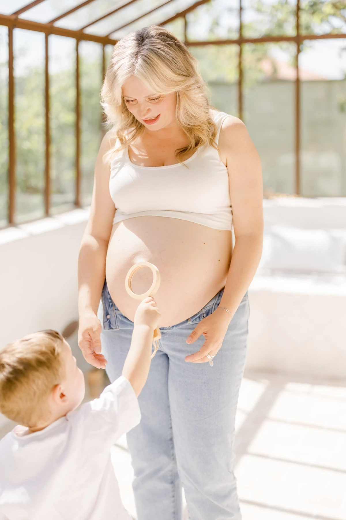 Séance grossesse en verrière : future maman partage un moment de complicité avec son enfant dans une lumière douce et naturelle