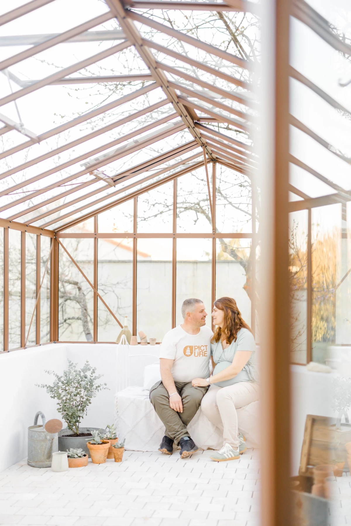 Séance grossesse en verrière : couple enlacé dans une serre lumineuse, ambiance douce et intimiste, Vendée