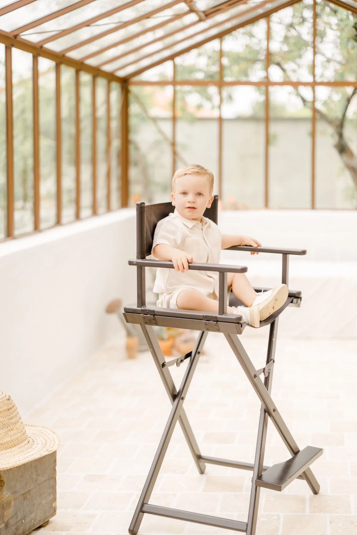 Séance famille au studio : jeune enfant assis dans une chaise haute vintage sous une verrière, ambiance douce et lumineuse