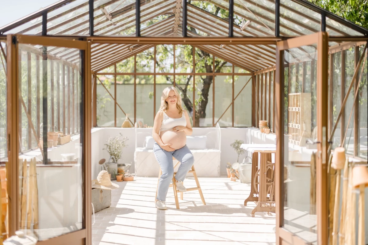 Séance grossesse en verrière : future maman assise dans un décor lumineux aux tons blancs et bois, ambiance douce et naturelle