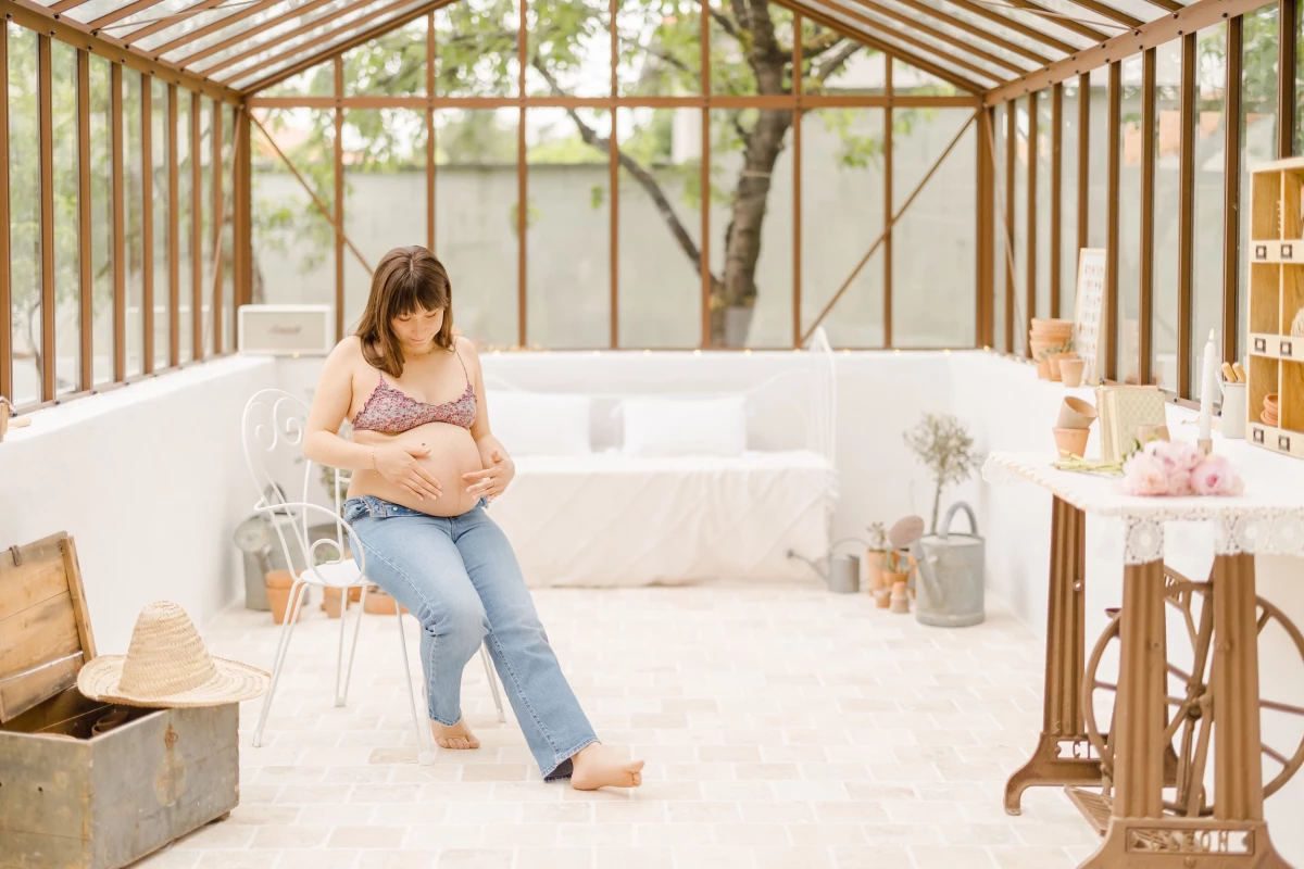 Séance maternité au studio : future maman berce son ventre dans une verrière lumineuse aux tons naturels et doux