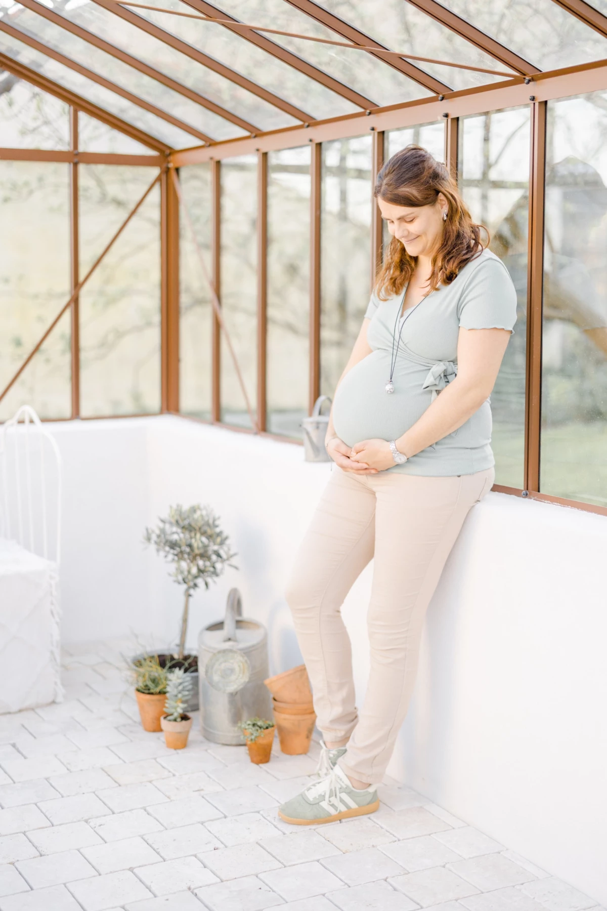 Séance grossesse en verrière : future maman caresse son ventre avec tendresse dans une lumière douce et naturelle en Vendée