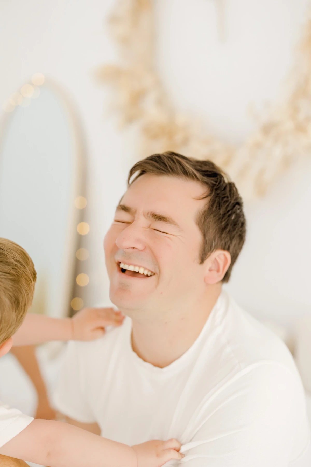 Séance grossesse au studio : le futur papa rit aux éclats dans une lumière douce, moment de complicité et de joie partagée en Vendée
