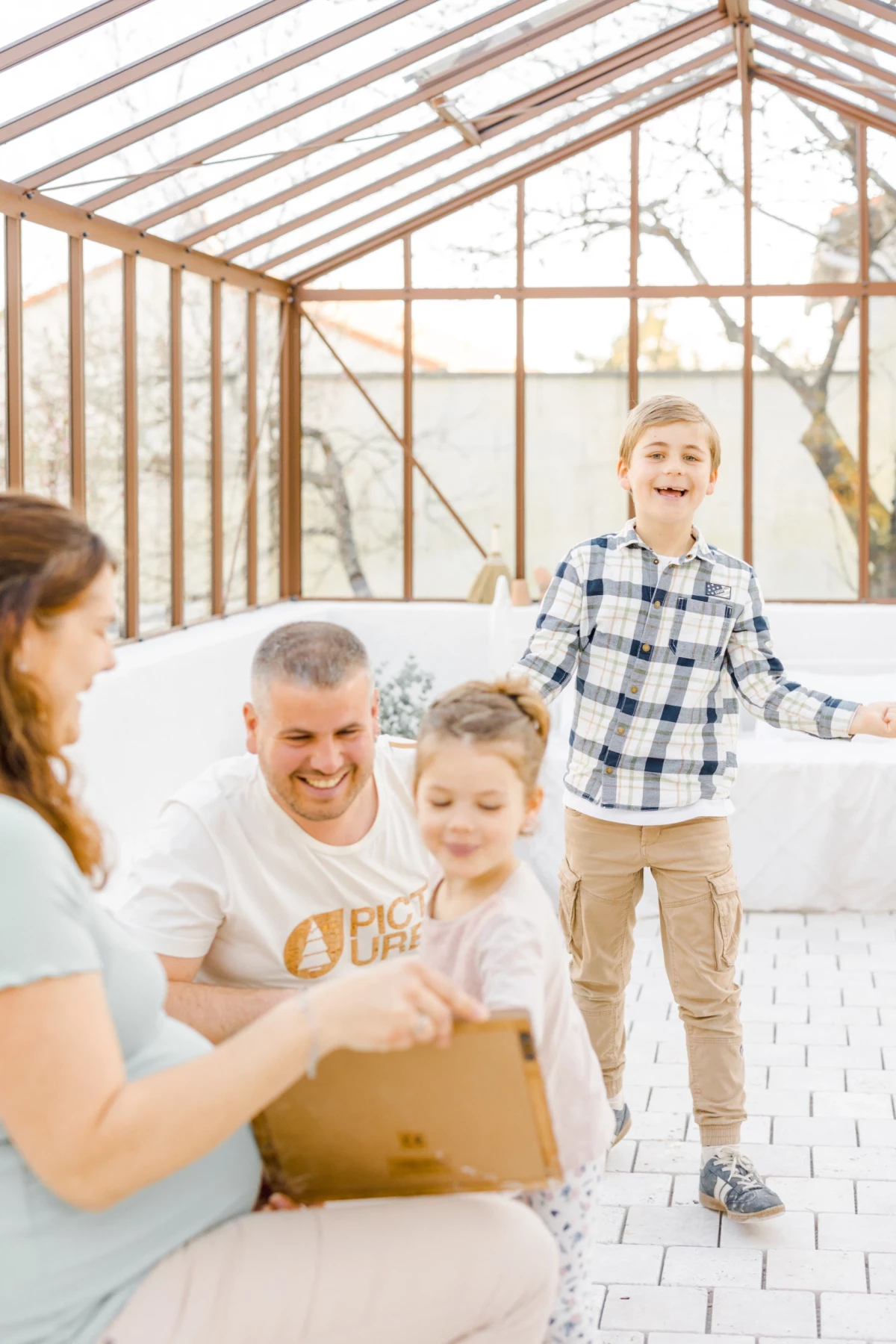 Séance grossesse famille : parents et enfants partagent un moment de joie dans une verrière lumineuse en Vendée