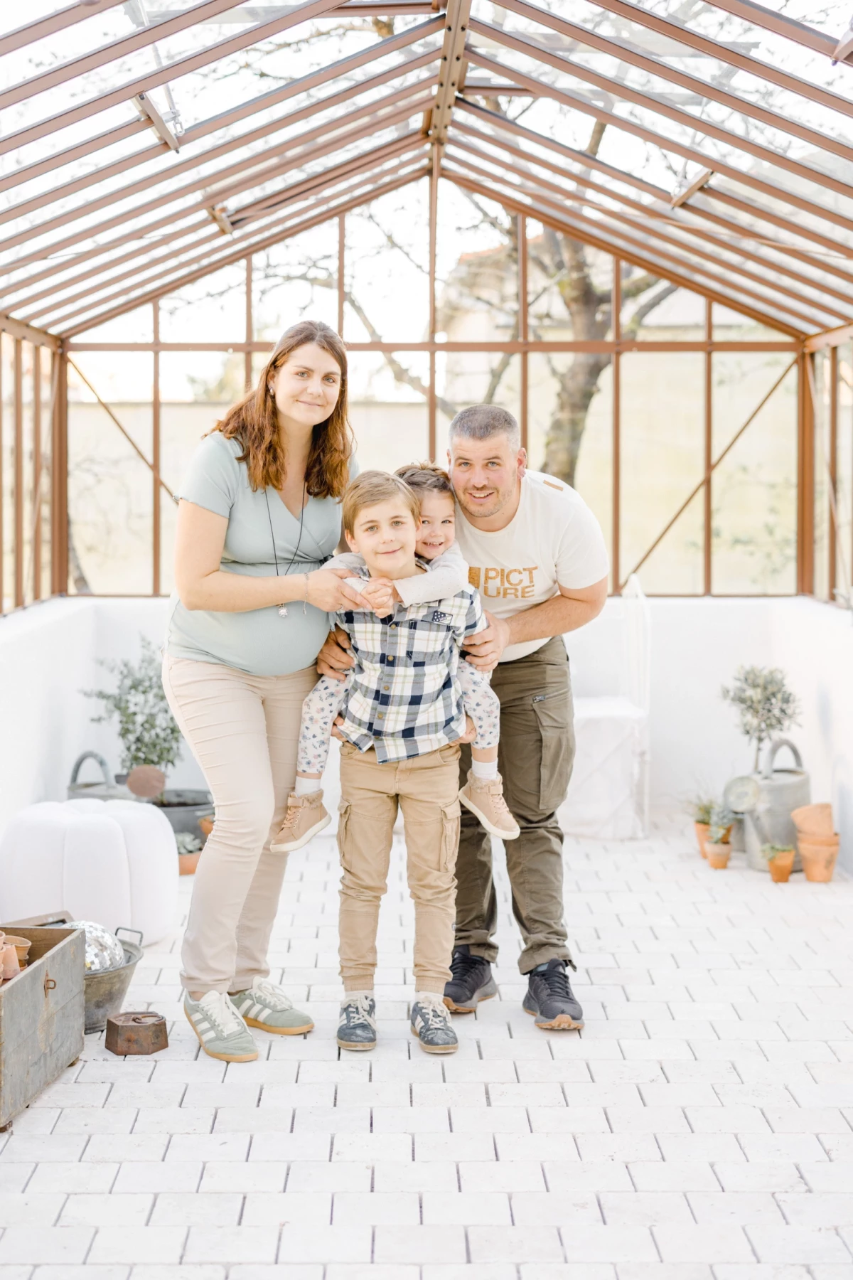 Séance grossesse en verrière : famille complice avec deux enfants, instant de bonheur partagé dans une lumière douce et naturelle