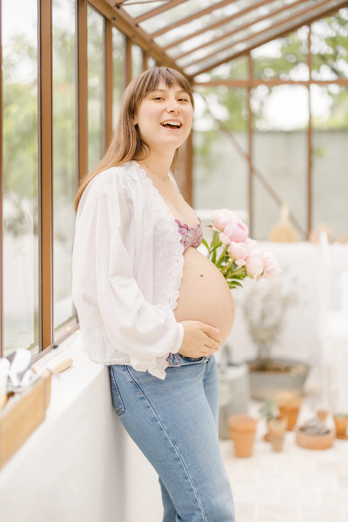 Séance grossesse en verrière : future maman rayonnante avec bouquet de roses, lumière naturelle douce et ambiance printanière