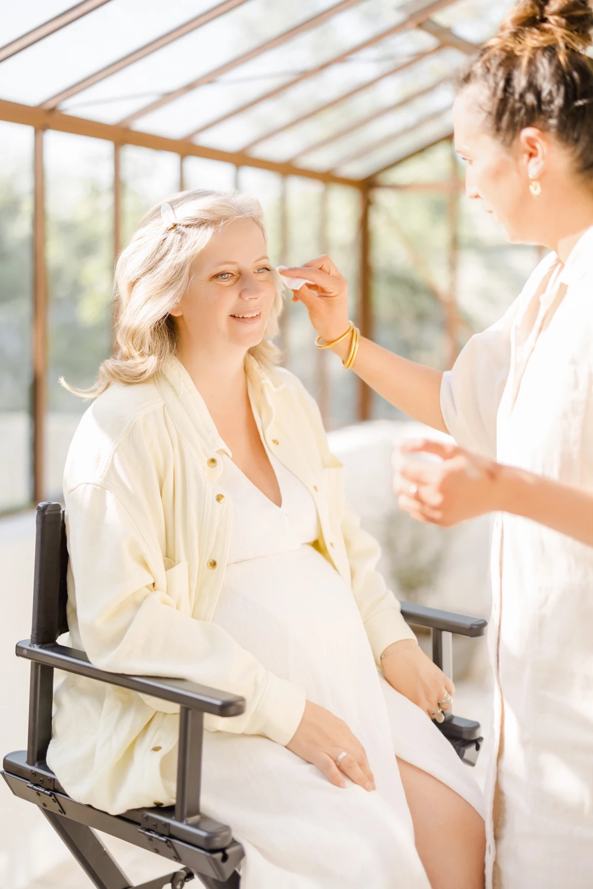 Séance grossesse au studio : future maman souriante lors des préparatifs maquillage dans une verrière lumineuse et douce