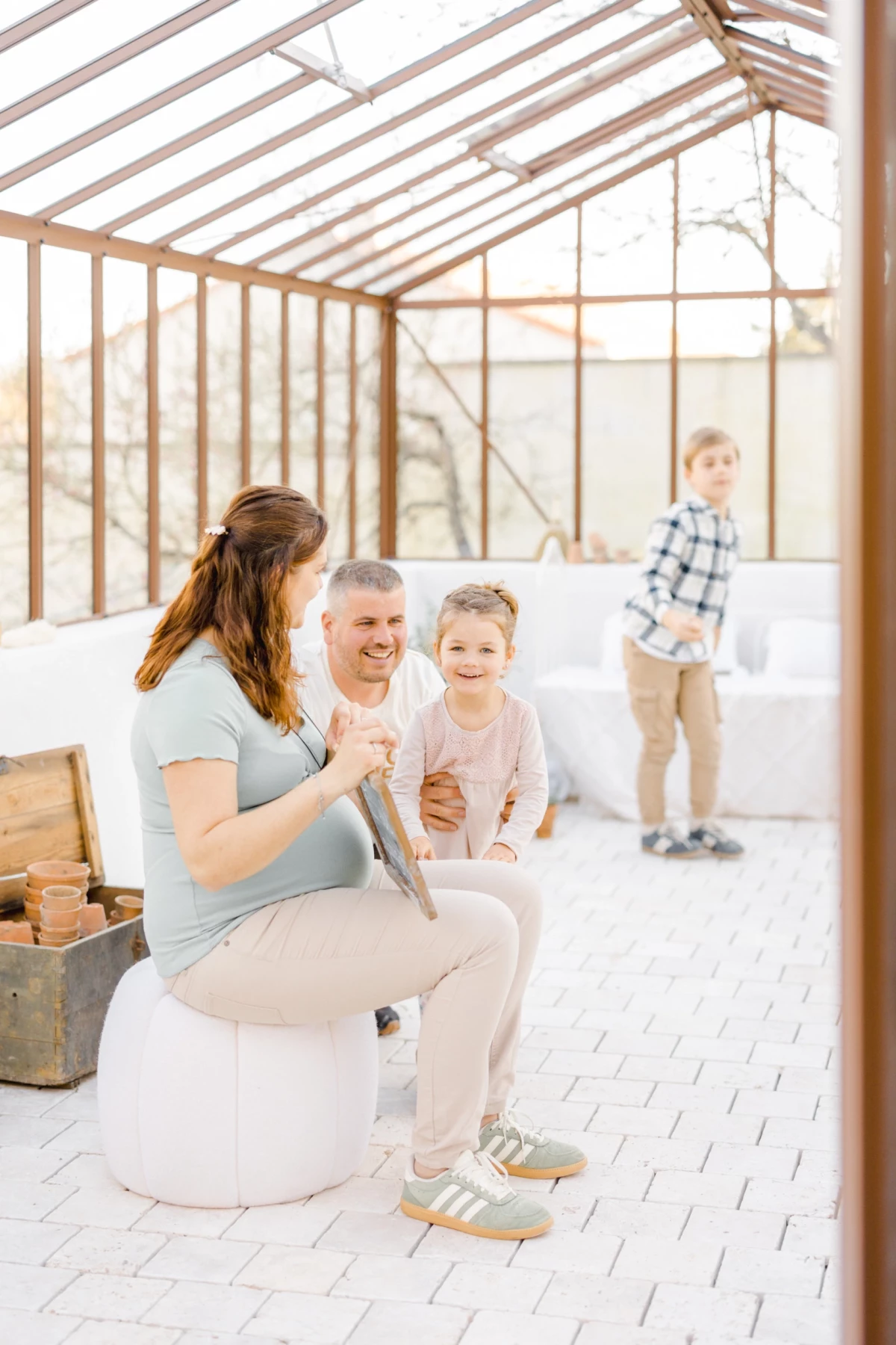 Séance grossesse en studio : future maman avec ses enfants dans une verrière lumineuse, instant de complicité familiale et tendresse
