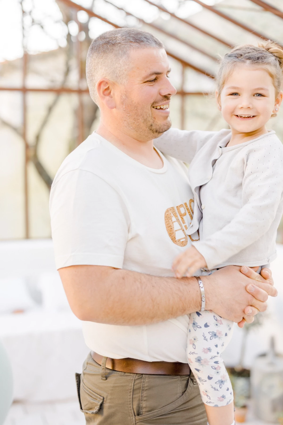 Séance famille en extérieur : père et enfant partagent un moment de complicité et de tendresse sous une verrière lumineuse
