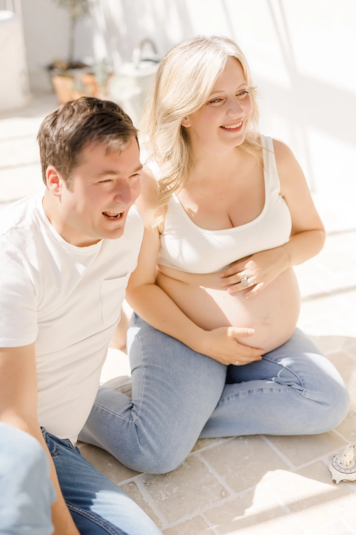Séance grossesse au studio : couple complice souriant, future maman caressant son ventre dans une lumière douce et naturelle
