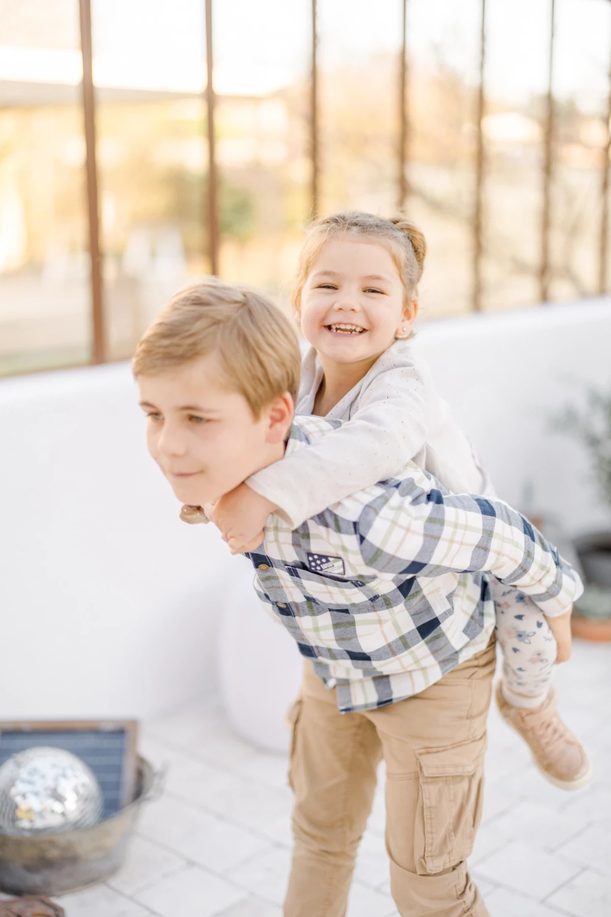 Séance famille dans une verrière : frère et sœur complices, moment de joie et de tendresse fraternelle dans la lumière naturelle