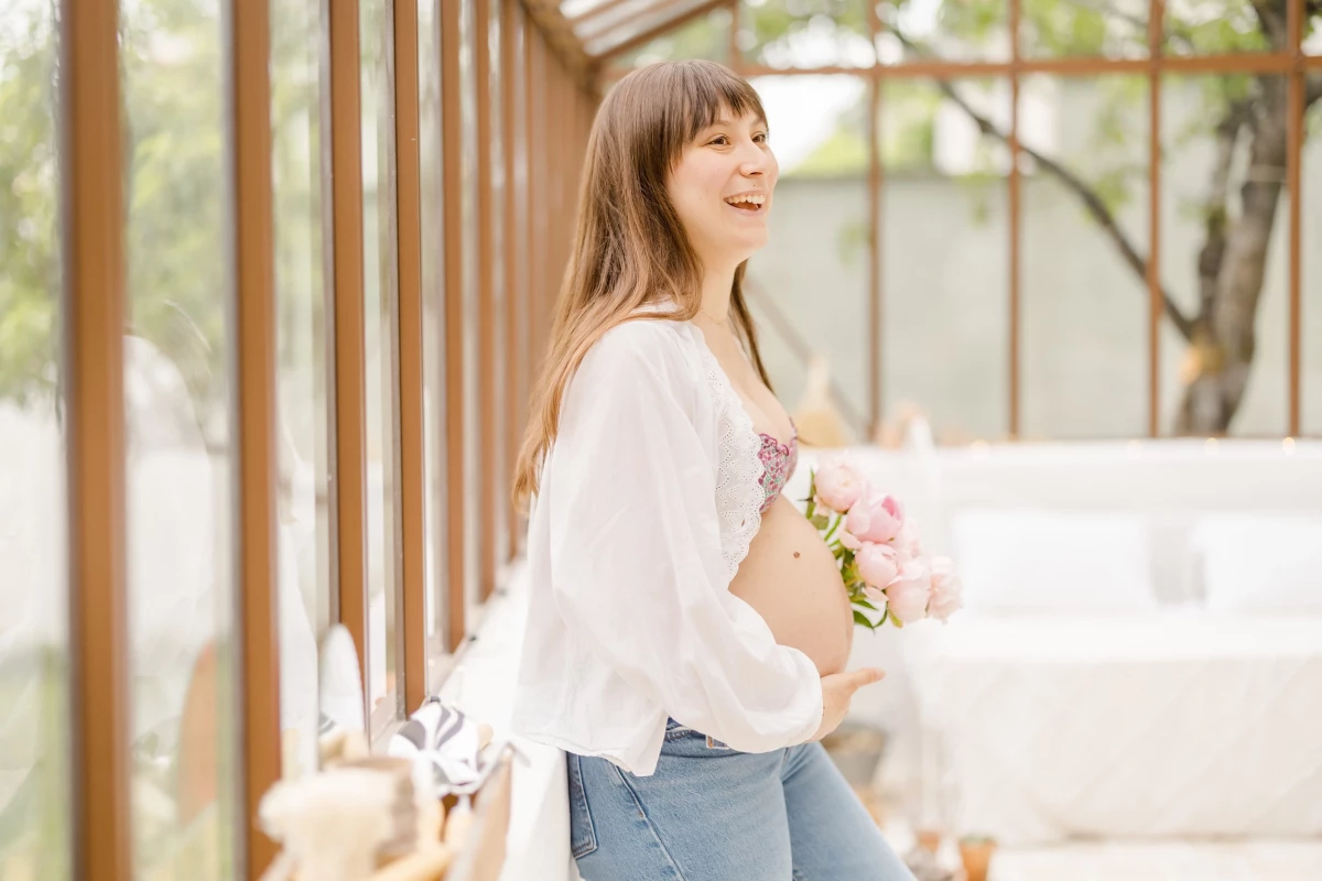 Séance grossesse extérieur : future maman souriante tenant un bouquet de fleurs roses dans une atmosphère printanière lumineuse