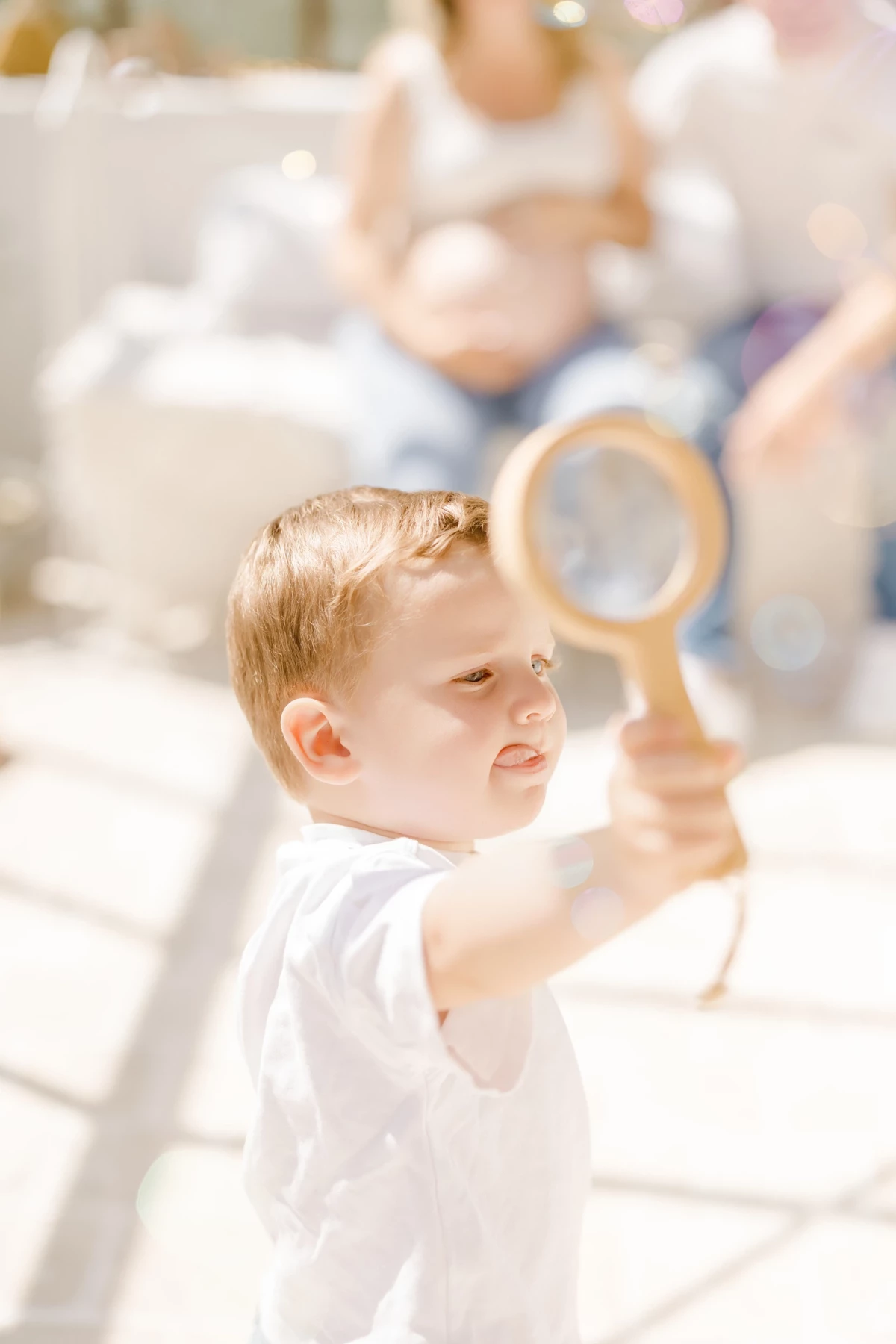 Séance famille en extérieur : jeune enfant joue avec une loupe sous le soleil, moment de découverte et de joie naturelle