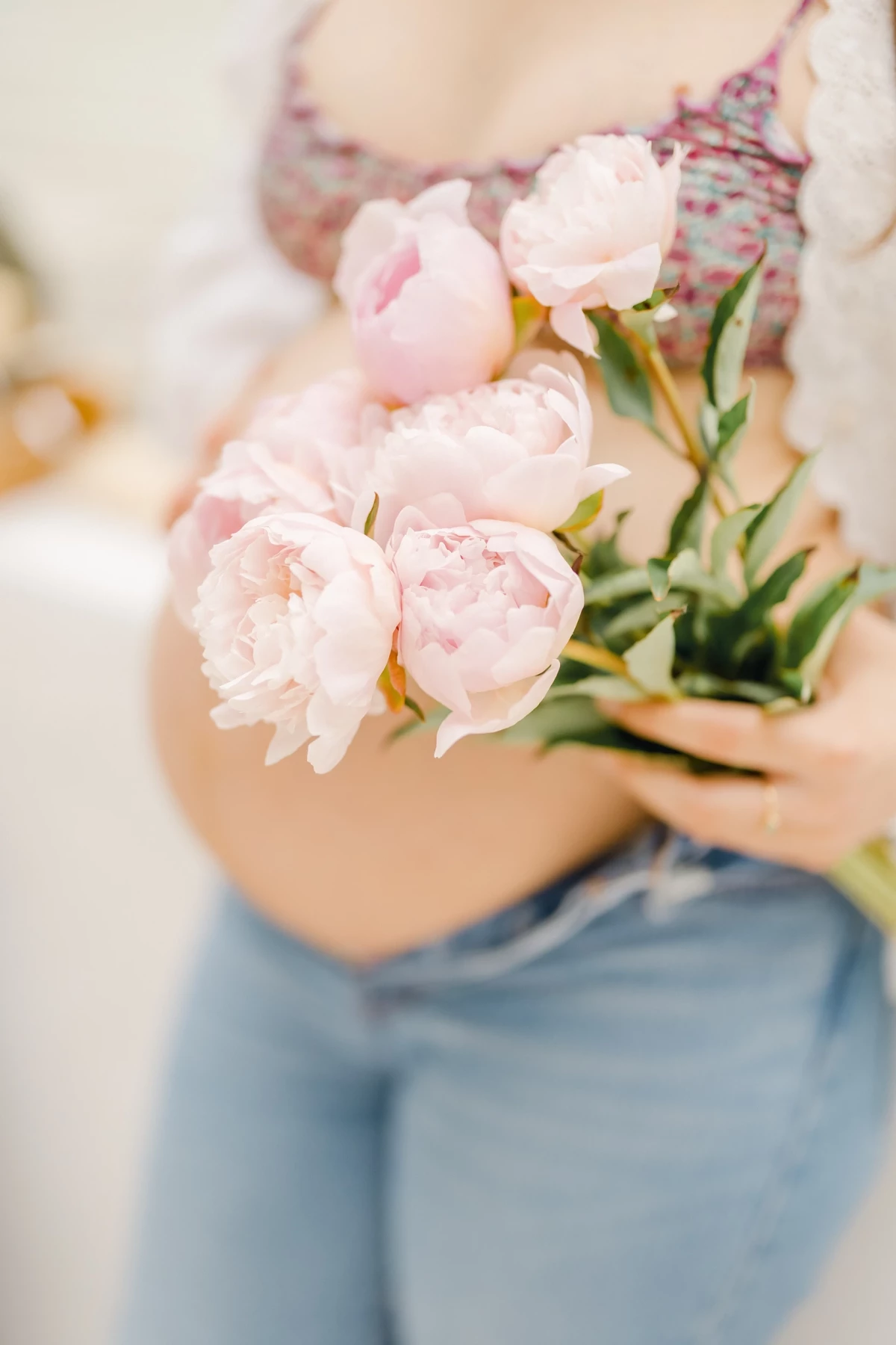 Séance grossesse au studio : future maman tient un bouquet de pivoines roses, douceur et attente sereine
