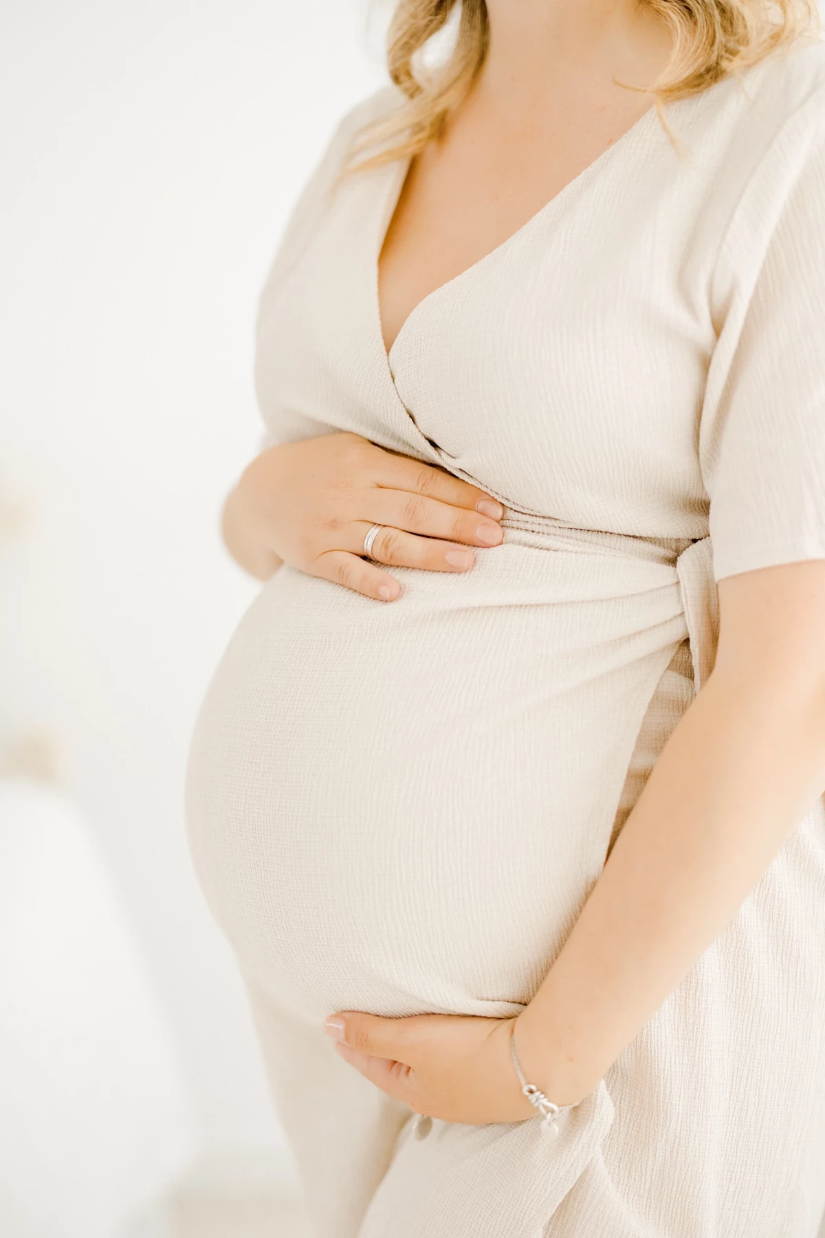 Séance grossesse en studio : future maman en robe beige caresse son ventre rond dans une lumière douce et intemporelle