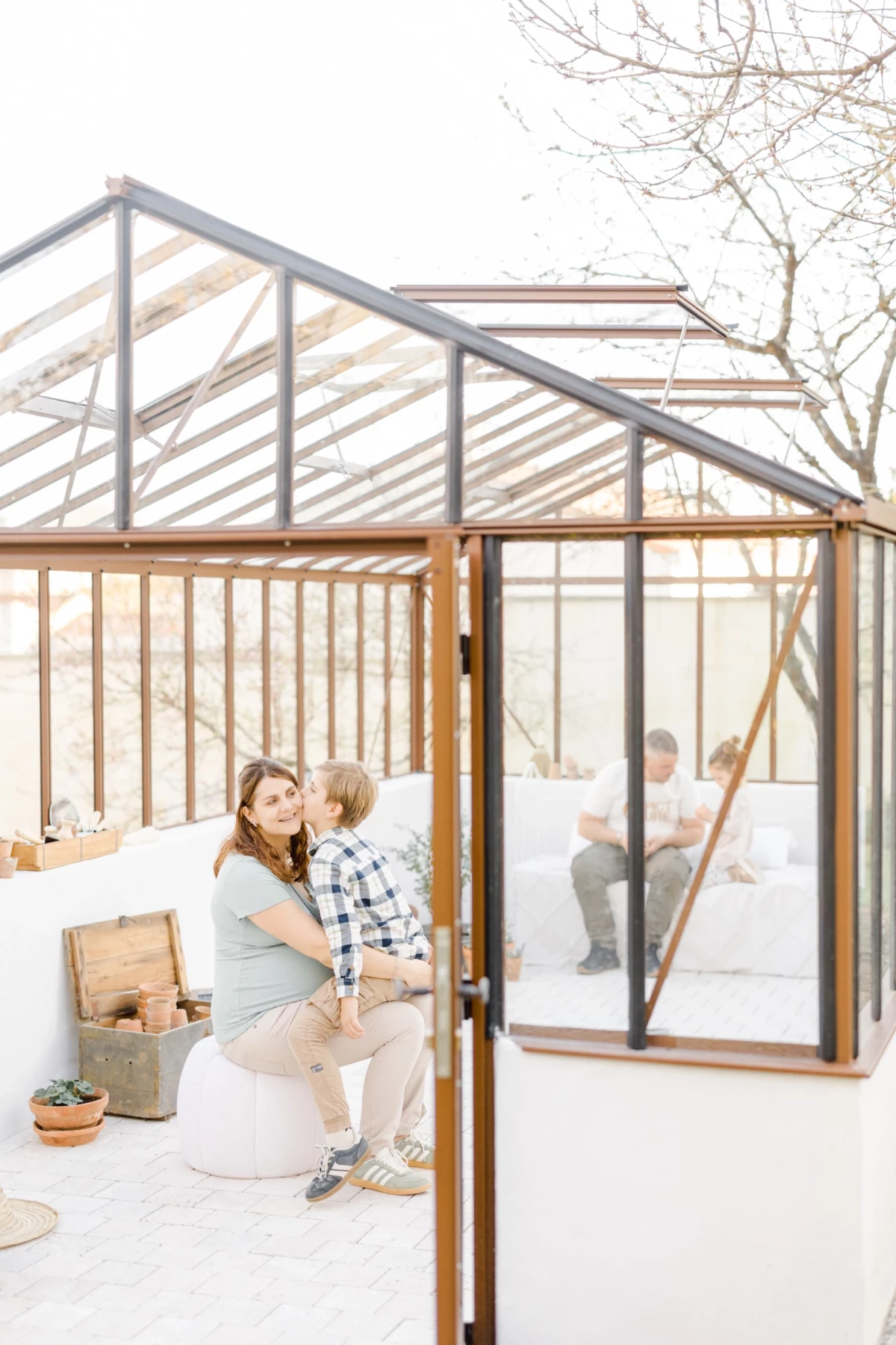 Séance grossesse en extérieur : future maman et son enfant partagent un câlin tendre dans une verrière baignée de lumière naturelle